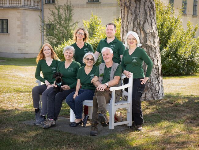Das Team von Vlasitz und Zodl sitzt mit grünene Vlasitz-und-Zodl-T-Shirts auf einer Bank unter einem Baum im Schatten
